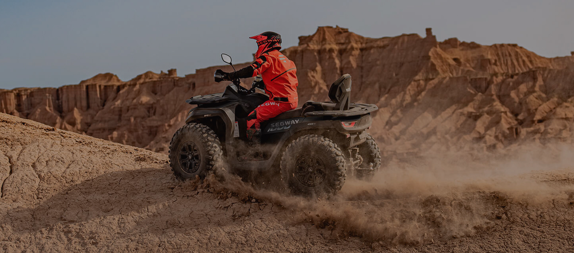 Person mit roter Jacke fährt Quad auf staubigem, felsigem Gelände