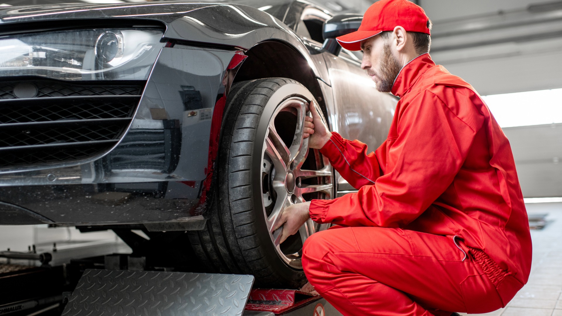 Kfz-Techniker kontrolliert Reifen und Rad eines Fahrzeugs in der Werkstatt